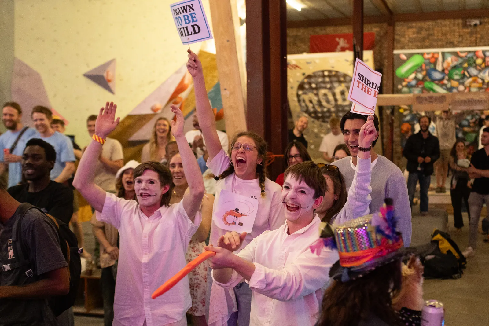 Spectators cheering and holding up signs as a climber tops out
