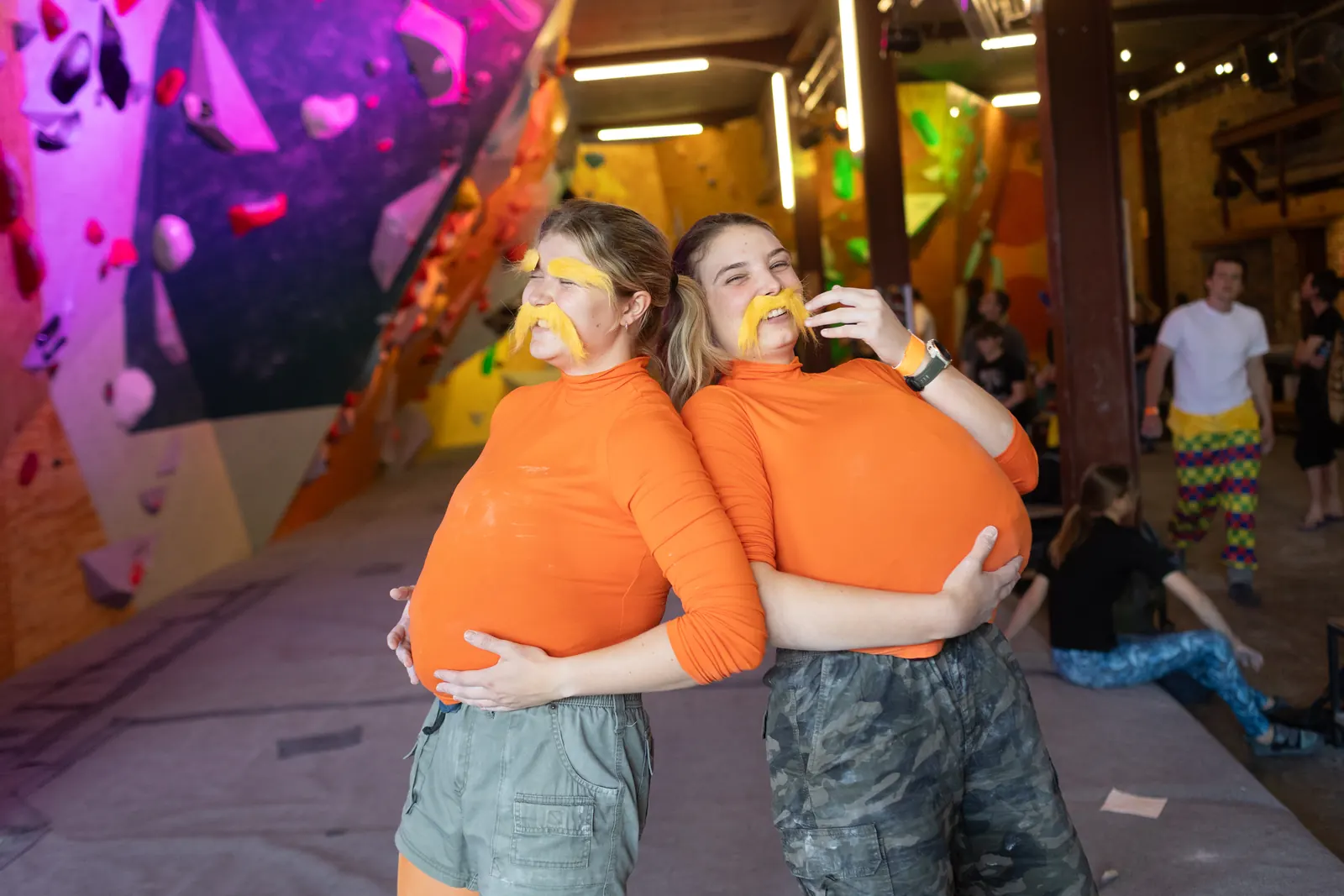 Two climbers in matching orange costumes posing on the mats