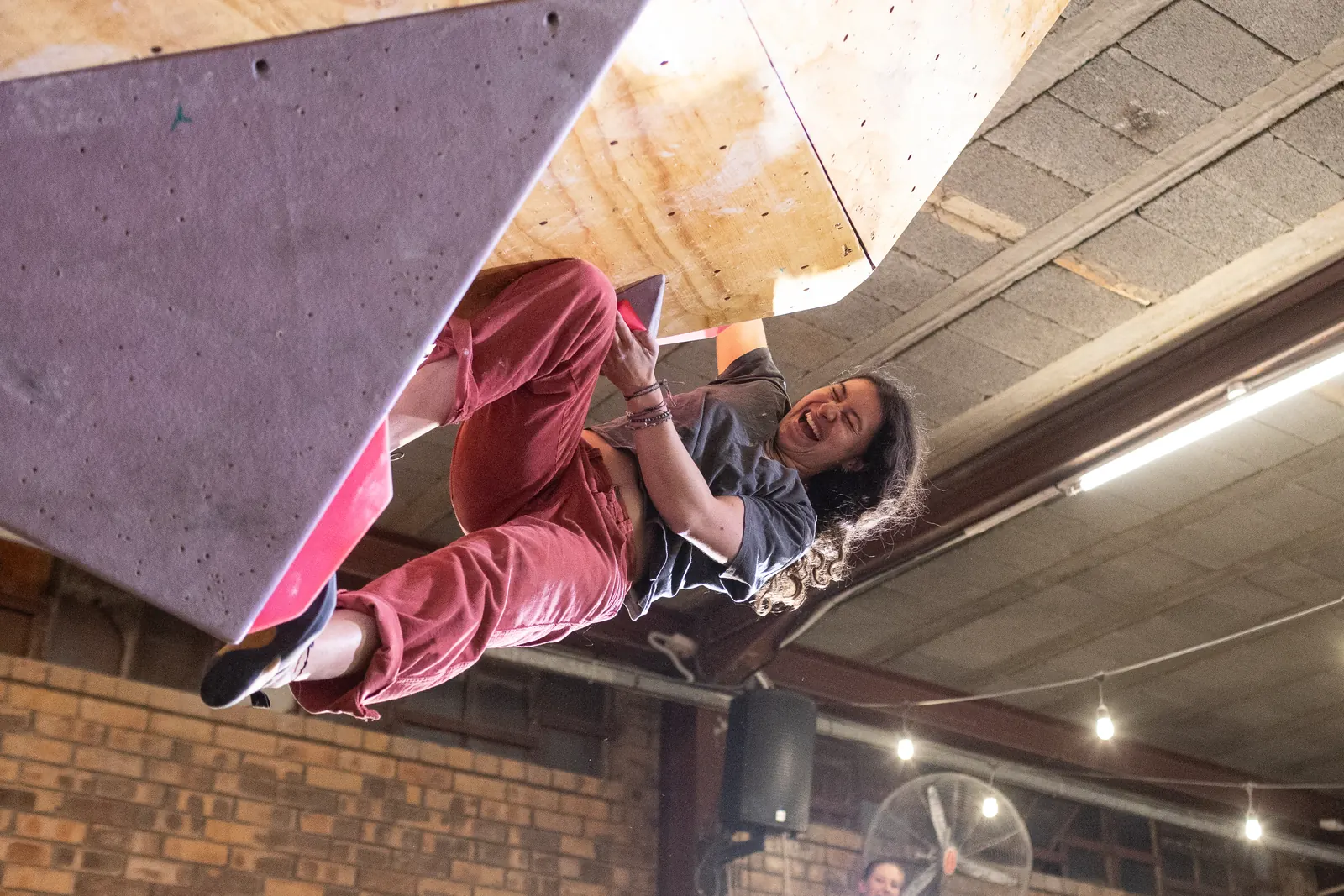 A finalist hanging from the roof of the comp wall in front of a packed crowd